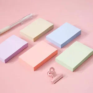 Close-up detail of colorful pastel sticky notes, cute binder clip, and pen on pink background.