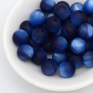 Gros plan de perles rondes bleues mates en oeil de chat dans un bol blanc pour bijoux DIY.