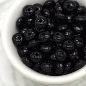 Close-up detail of glossy black wheel spacer beads in a white bowl for DIY jewelry making accessories.