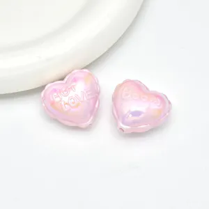 Detailed shot of pink iridescent acrylic balloon heart beads with embossed letters for DIY jewelry.