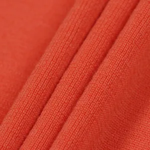 Close up view of soft coral orange knit fabric texture showing fine woolen sweater details.