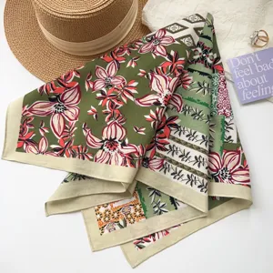 Gros plan de détail d'un foulard carré floral vert stylisé avec chapeau et carte.