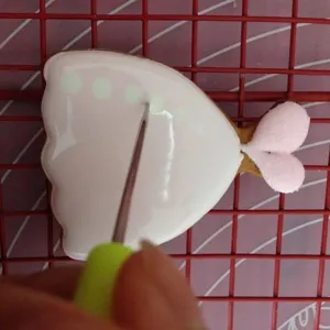 Detail shot of fondant cookie icing scribing needle tool with green handle in use.