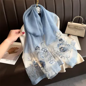 Silk embroidered scarf detail close-up, elegant blue floral design on sheer fabric, luxury accessory.