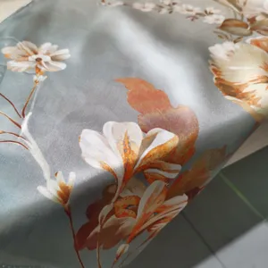 Close up detail of grey blue silk scarf featuring elegant orange floral print and smooth texture.