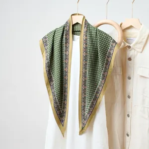 Détail de foulard triangulaire en soie à motifs verts, élégant accessoire de superposition.