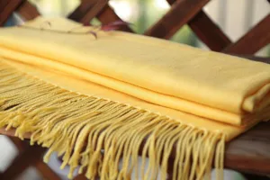 Vista detallada de una bufanda de lino amarillo mostaza con flecos, textura suave.