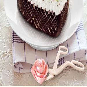 Nahaufnahme Detail der rosafarbenen Plastikkuchendekorationsschere mit einer Cremeblume.