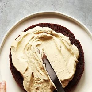 Dettaglio di una spatola per dolci in acciaio inox che stende la crema su una torta al cioccolato.
