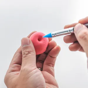Close-up of a blue silicone clay shaping pen smoothing a pink modeling clay ball surface.