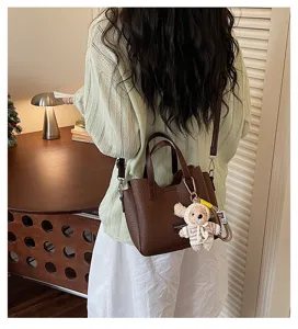 Detail view of a stylish brown leather crossbody bag with cute plush charm for women.
