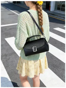 Black textured leather shoulder bag detail with silver metal buckle, stylish street style look.