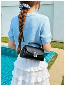 Detail view of a stylish black leather shoulder bag with metallic buckle worn by a model.