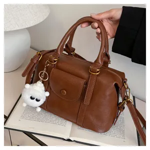 Brown leather handbag detail view, featuring front pocket design and cute fluffy keychain charm.