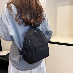 Back view of a casual minimalist black nylon backpack, featuring multi-layer storage and zippers.
