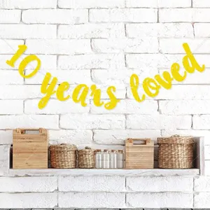 Detail shot of sparkling gold 10 years loved letter banner hung on white brick wall.