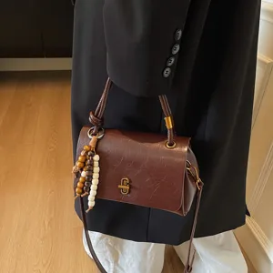 Minimalist brown shoulder bag with wood bead charm, stylish commuter handbag for women.