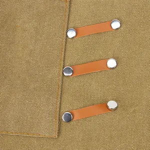 Close-up detail of khaki canvas work apron featuring leather straps and metal rivet buttons