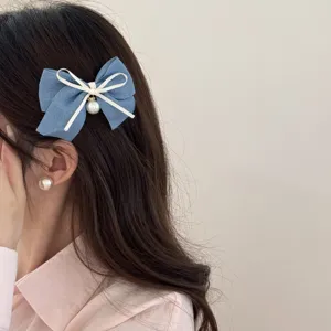 Detail view of the denim blue bow hair clip showcasing the cute white ribbon and pearl detail.