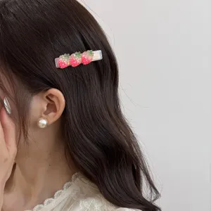 Gros plan d'une jolie pince à cheveux avec de jolies fraises rouges en résine brillante.