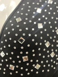 Black rhinestone dress fabric detail close-up, elegant sparkling crystals on textile.