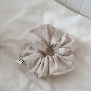 Close-up detail of a soft pink polka dot scrunchie, showing fine fabric texture and neat label.