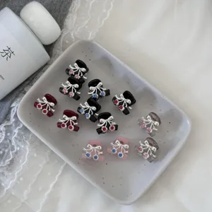 Detail view of cute mini rhinestone cherry hair claws displayed on a ceramic tray for styling.