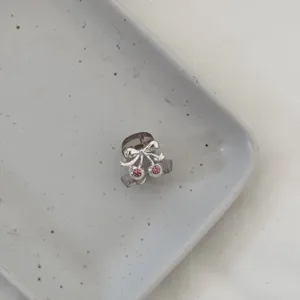 Close-up detail of a cute mini hair claw clip featuring a silver bow and pink rhinestone cherry.