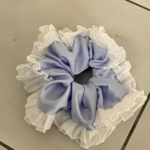 Blue satin hair scrunchie featuring elegant white lace ruffle trim detail close up.
