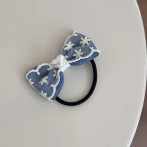 Close-up detail of blue denim bow hair tie with white lace embroidery and heart bead.