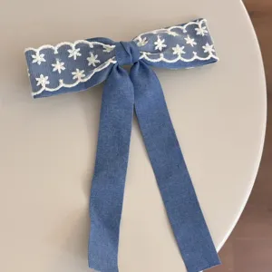 Blue denim hair bow featuring delicate white lace trim and long streamers for sweet styles.