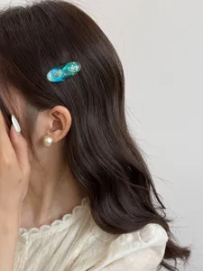 Detail close-up of the ocean blue resin hair clip with shell texture, worn on styled dark hair.