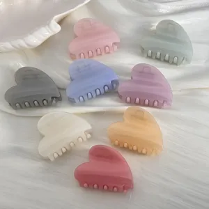 Vue détaillée de pinces à cheveux en forme de cœur pastel sur un tissu de soie blanche.