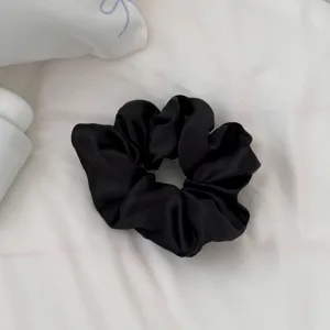 Detalle de coletero de satén negro, elegante accesorio para el cabello de mujer, diseño liso.