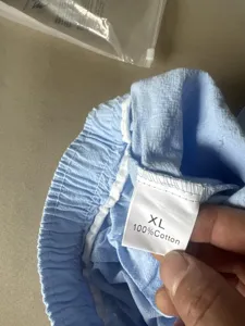 Detail shot of men's casual trousers elastic waistband and size tag showing 100% cotton fabric.