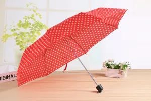 Primo piano sul dettaglio dell'ombrello pieghevole rosso a pois con design grazioso.