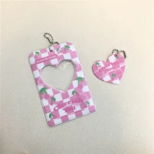 Pink checkered acrylic photocard holder detail with heart cutout and cherry pattern keychain.