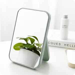 Minimalistische make-upspiegel op tafel met opvouwbare standaard en lichtgroen kader voor dagelijks.