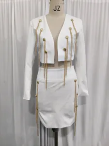 Weißes Zweiteiler-Set mit langärmeligem Blazer und Rock mit goldenen Ketten und Quasten.