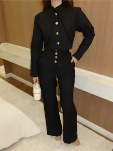 Detailansicht des eleganten schwarzen Stehkragen-Tops mit goldenen Knöpfen und hoher Hose.