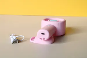 Detailansicht eines rosa tragbaren Mini Handventilators mit USB Ladekabel auf beigem Tisch.