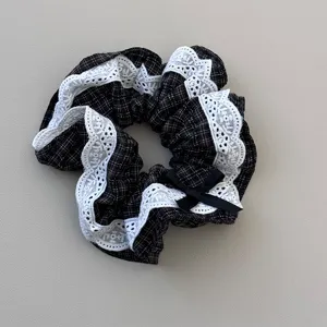 Close-up detail of black plaid hair scrunchie featuring elegant white lace trim and bow.