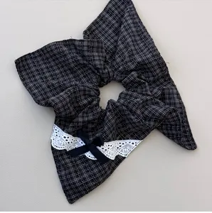 Detail view of British style plaid hair scrunchie with white lace trim and cute black bow.