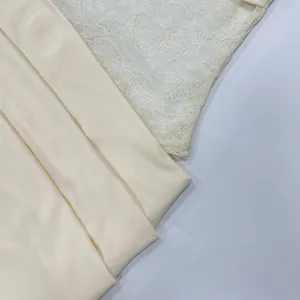 Close-up detail shot of elegant women's dress fabric with lace patchwork and smooth beige material.