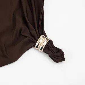 Gros plan sur le détail de la robe, tissu marron lisse et élégante boucle en anneau métallique doré.