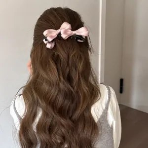 Vista detallada de una pinza para el pelo con lazo de satén rosa en cabello ondulado, elegante.