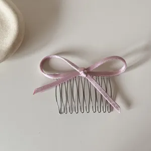Vista detallada de una peineta metálica con lazo rosa, accesorio para el cabello minimalista.