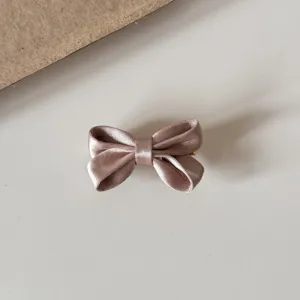 Satin bow hair clip detail shot, elegant pink color, soft fabric texture with metal clip.