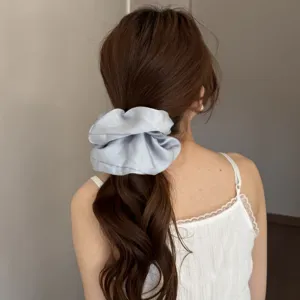 Detailed view of a light blue satin hair scrunchie worn on brown hair, soft glossy texture.