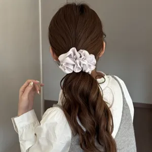 Detailed shot of a stylish light grey satin scrunchie worn on brown hair, elegant and versatile.